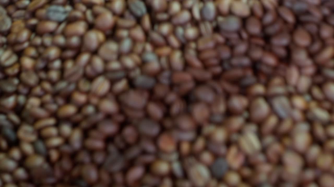 Sfondo ravvicinato testurizzato di chicchi di caffè misti con variazioni di marrone naturale, in rotazione in una tramoggia di metallo.