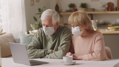 Pareja-De-Ancianos-Con-Máscaras-Hablando-En-Una-Llamada-Web-En-Una-Laptop-En-Casa