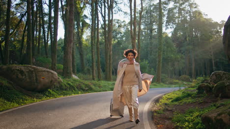 confident girl walking forest road in autumn evening with suitcase. explorer