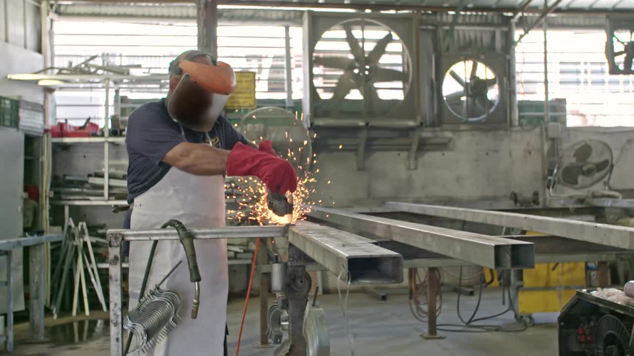 Cámara lenta de un trabajador usando una amoladora de metal con chispas volando en un taller de metal