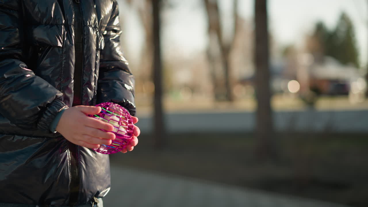 손에 보라색, 박이는 물체를 들고 있는 아이의 클로즈업, 그들이 그것을 버리기 직전에 찍은 사진, 아이는 반이는 검은색 재을 입고 있고, 배경은 흐릿합니다.