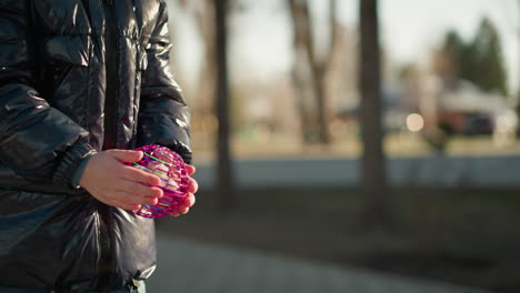 a close-up of a child holding a purple, blinking object in his hands, captured just before they throw it away, the child is dressed in a shiny black jacket, and the background is a blurred