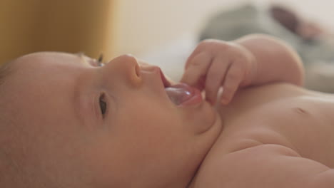 happy baby looking with curiosity laying on his back, sticks his fingers in mouth