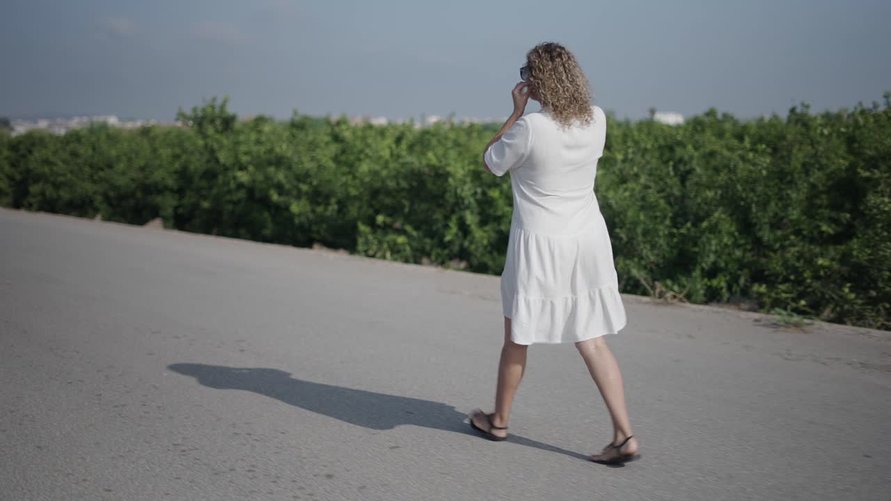 Woman Walking on a Road Through a Tree Plantation