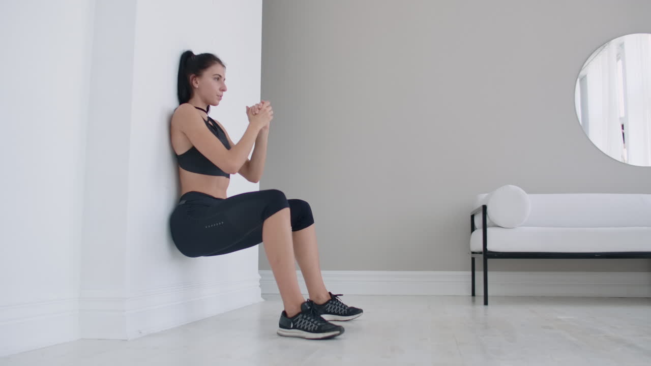 una mujer en una posición estática realiza un ejercicio agotador apoyándose en una pared en una posición sentada. entrenamiento de resistencia.