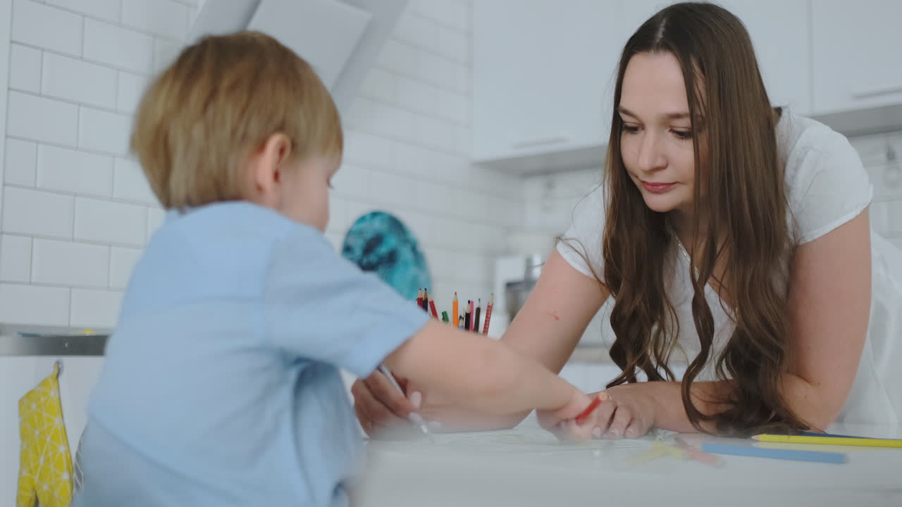 mamá ayuda a dos hijos a realizar tareas preescolares para dibujar un dibujo a lápiz sentado en la mesa en la casa
