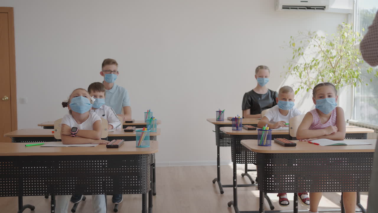 교사의 질문에 대답하기 위해 손을 들어보세요. 코로나19 대유행 기간 동안 학교에서 마스크를 쓴 다민족 어린이 그룹.