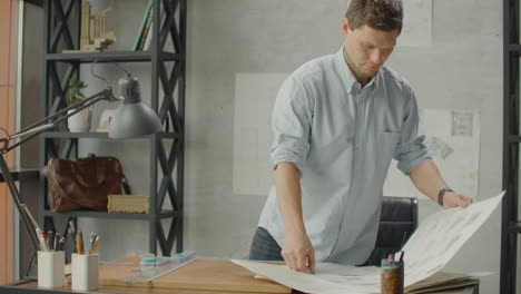 engineer works in a bright office with a large window concentrates and draws blueprints. workplace of an architect or designer: loft style minimalistic interior drawings and coffee on the table.