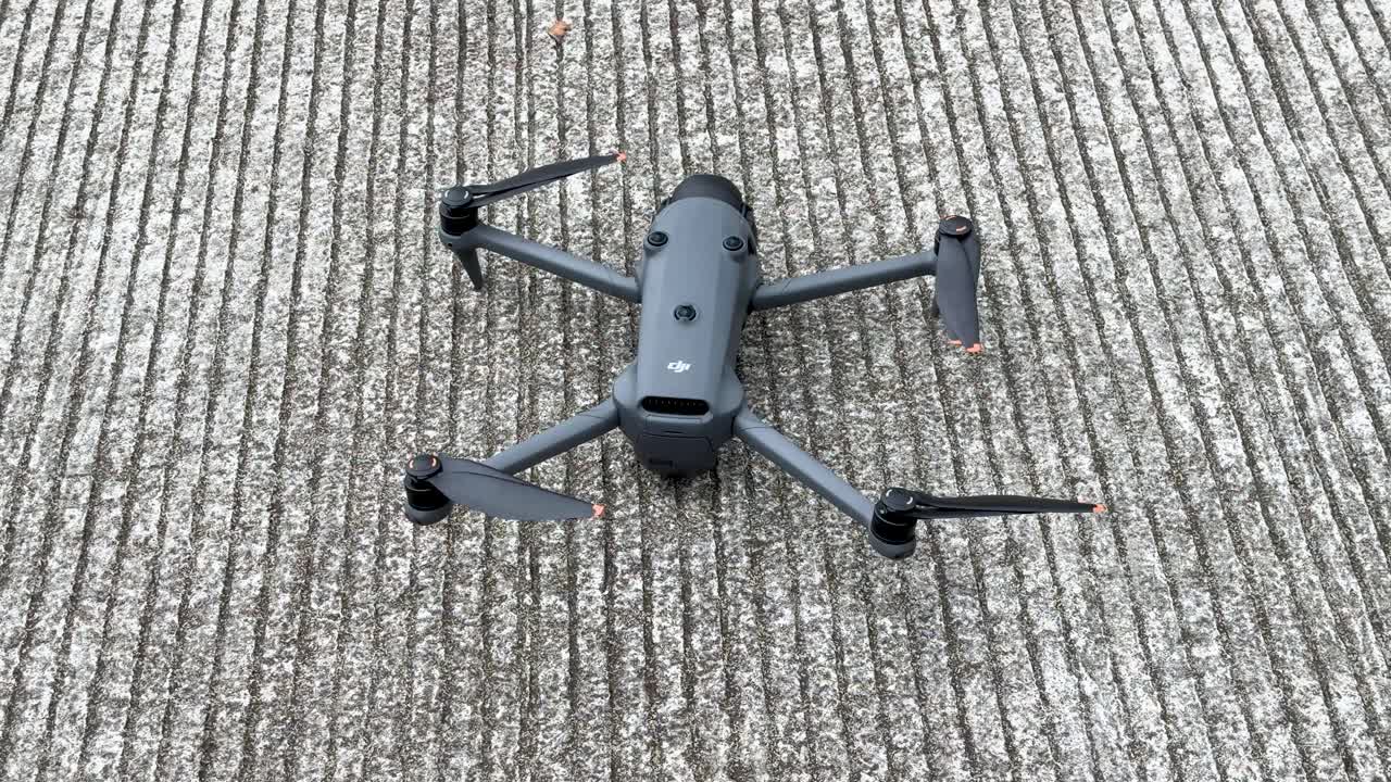 Korkeasta kulmasta otettu staattinen kuva tummanharmaasta nelikopteridronesta lepäämässä uritetulla betonilla.