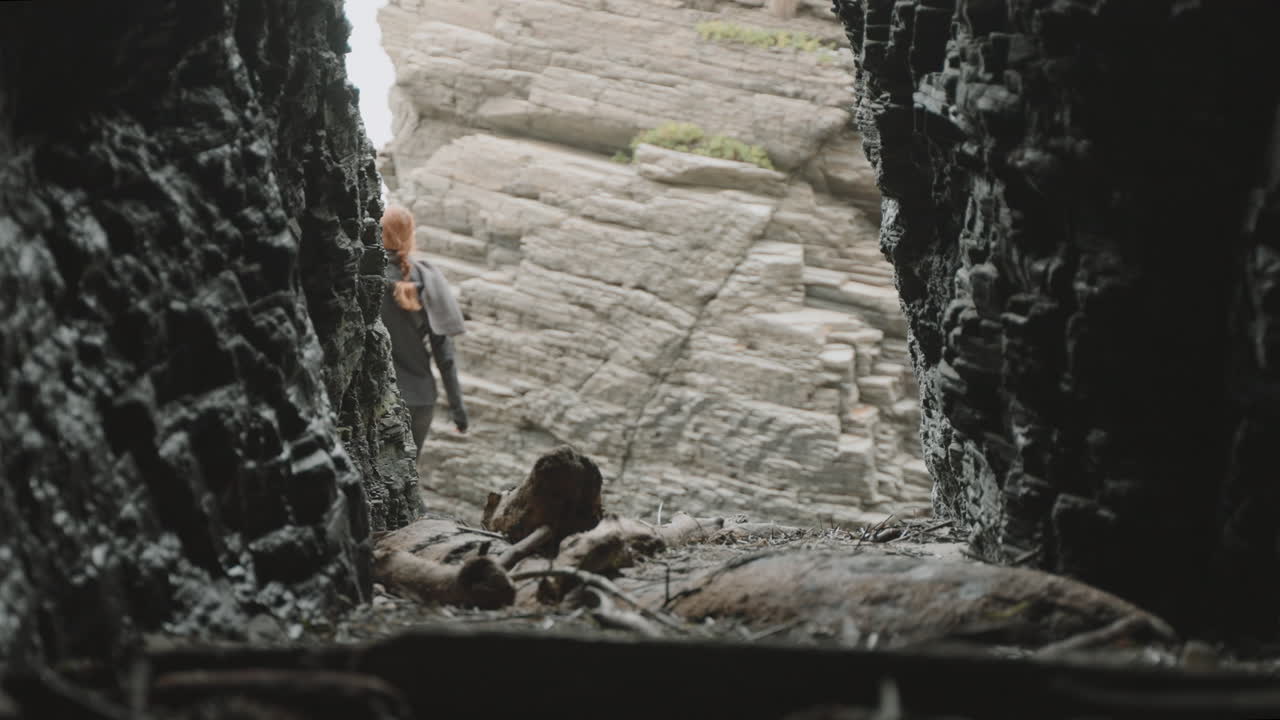 A person exploring a cave and emerging into a rocky landscape