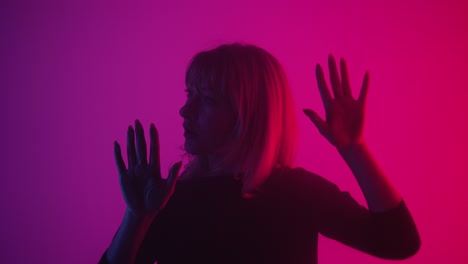 woman emerges from smoke and touches glass with palms - pretty young woman emerges from the smoke and touches the glass with her palms. blonde examines glass and slides her hands over it with interest and surprise. model poses in dark studio with pink and purple lights in the background. close up