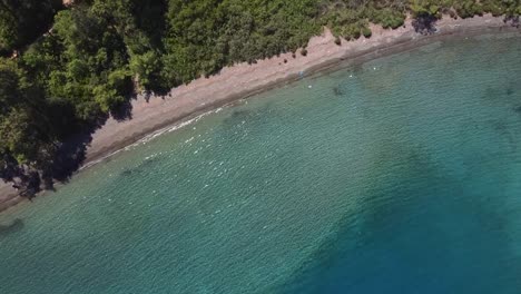 Top-down-aerial-view-on-a-narrow-stretch-of-beach-between-a-turquoise-calm-bay-and-a-lush-green-forest-in-southern-Turkey