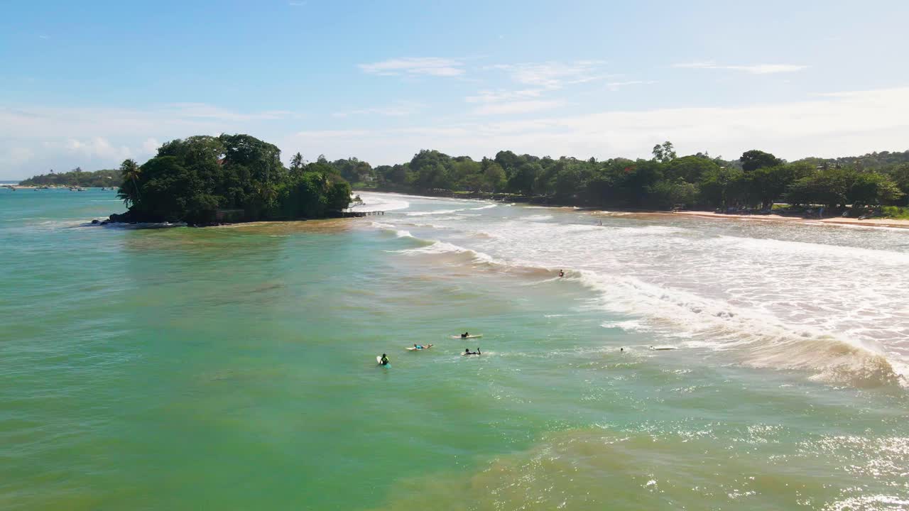 Drone footage showcasing Taprobane Island and surfers catching waves at Weligama Beach, Sri Lanka.