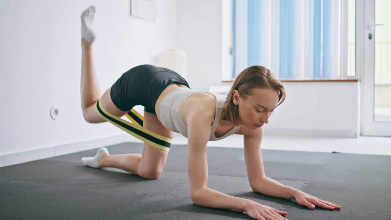 힘을 얻은 여자가 집에서 체조를 연습하면서 다리를 구부리고 몸을 펴고 있습니다.