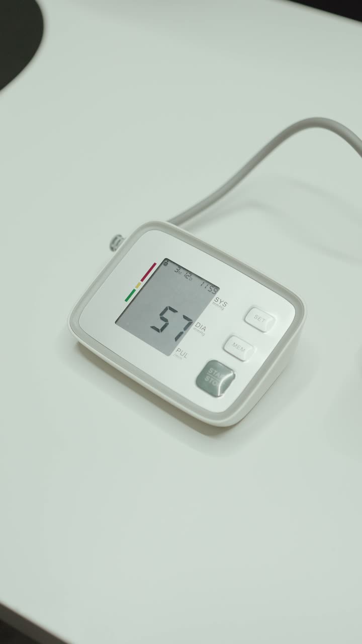 Primo piano di un misuratore di pressione digitale che mostra la lettura su un tavolo in ambiente medico, in verticale.