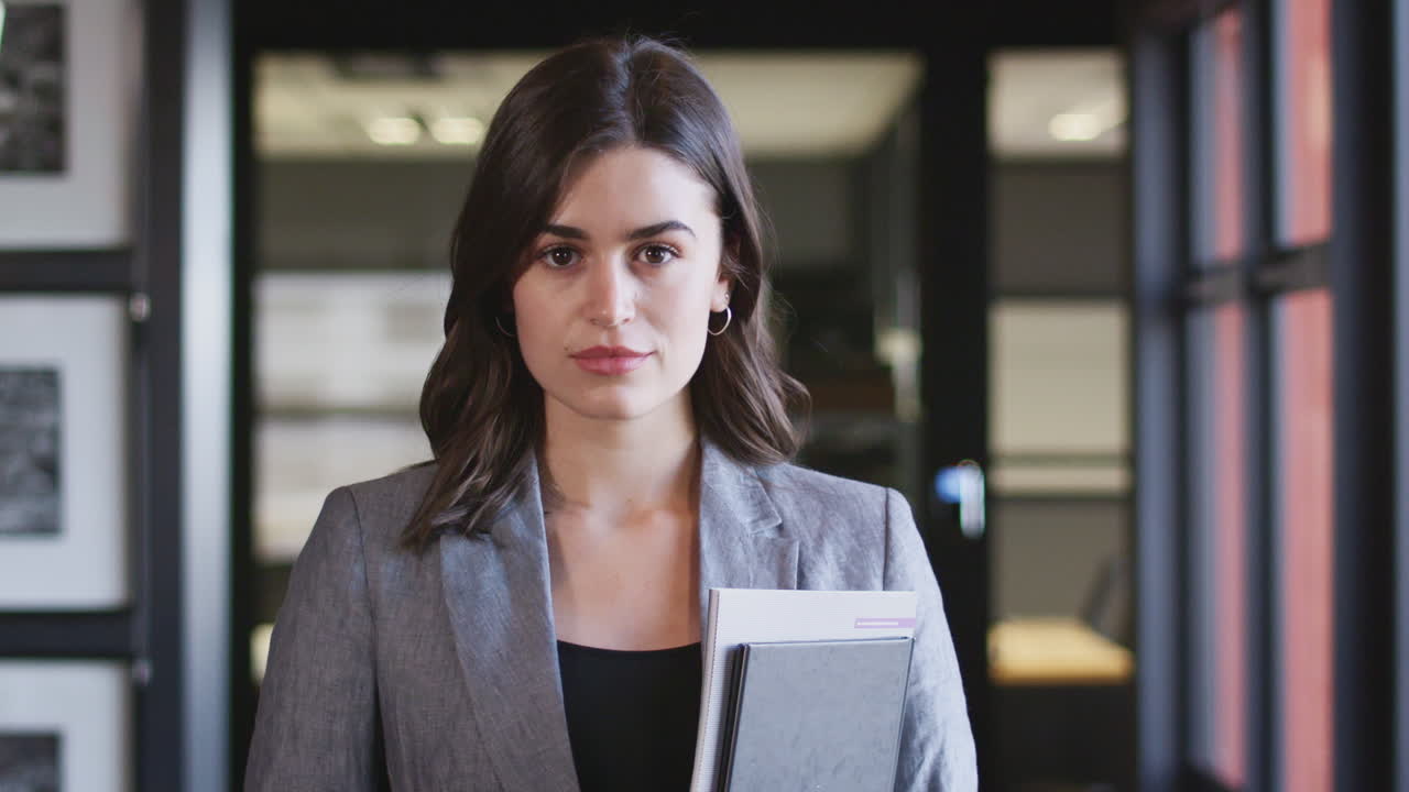 Dark haired, confident young businesswoman holding documents, turns and smiles to camera, close up