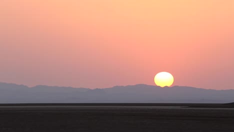 Amanecer-Frío-Temprano-En-La-Mañana-En-Un-Clima-Cálido-De-Desierto-En-El-Centro-De-Irán-El-Punto-Más-Caliente-De-La-Tierra-El-Sol-Se-Eleva-Sobre-El-Paisaje-Montañoso-Cielo-De-Color-Naranja-Y-Superficie-Plana-Del-Desierto-Viajando-Con-Camper