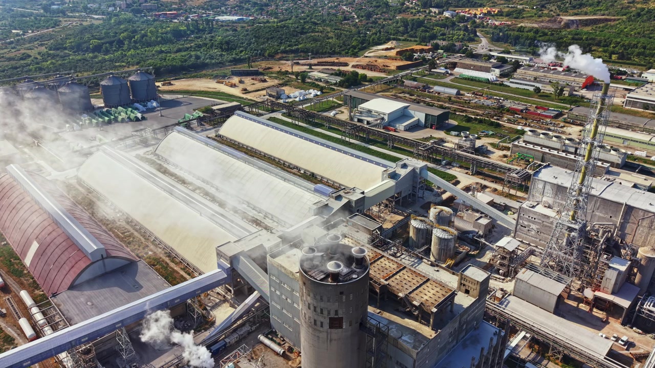 Large industrial complex with multiple buildings and smoke coming from stacks in a rural area during daytime