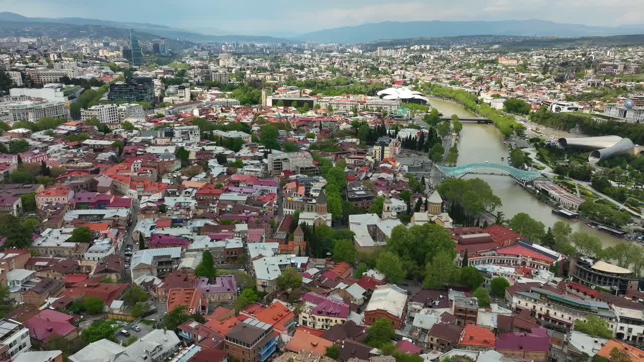 A broad aerial perspective over the heart of Tbilisi, showing dense residential areas, winding river, and the mix of old and modern buildings