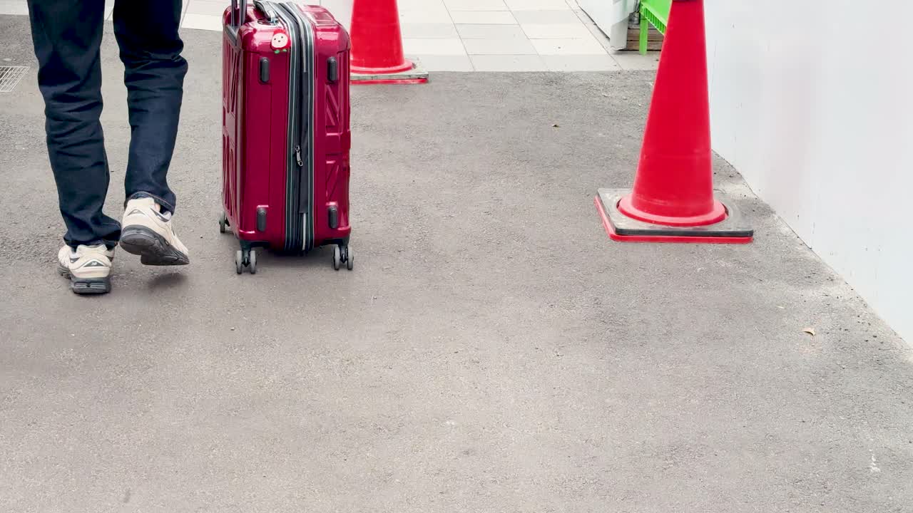 Toma de ángulo bajo de un viajero arrastrando equipaje por una calle pavimentada en Tokio.