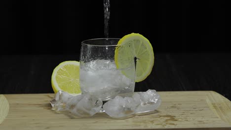 Pours-lemon-juice-into-glass-with-ice,-thyme-and-lemon-slices