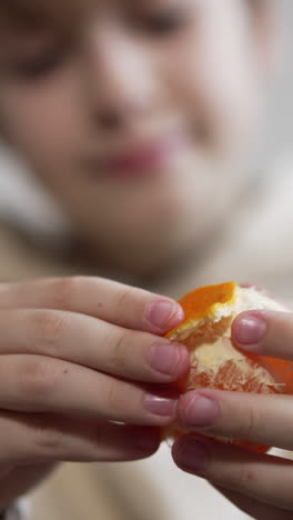 unknown boy peeling the tangerine in front of camera. teenager rips the fruit into pieces ready to eat. close up. blurred backdrop. vertical video