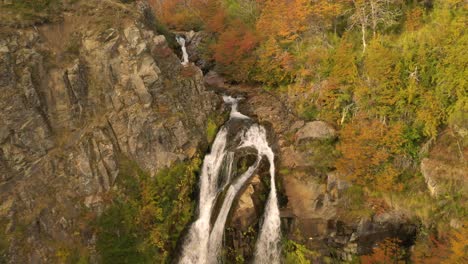 cinematic aerial shot of a waterfall and revealing an autumnal woodland in patagonia, argentina