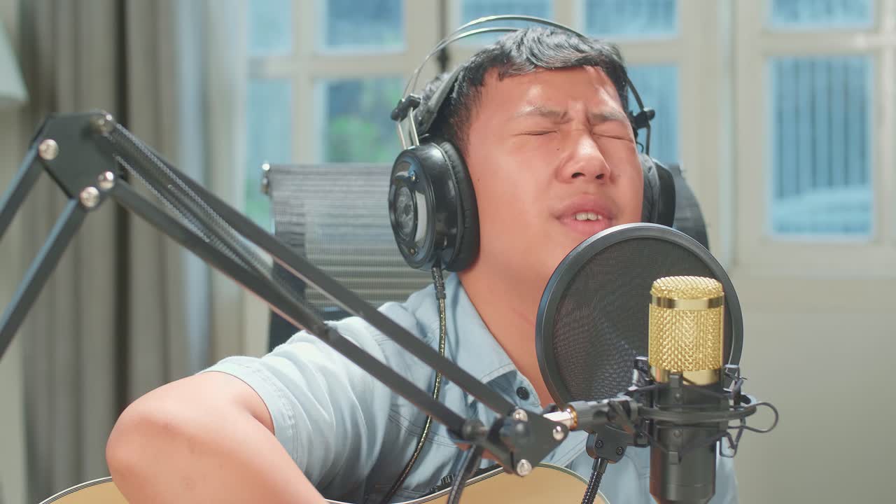Young Asian Boy In Headphones Playing The Guitar And Singing Into Microphone While Recording Podcast In Studio
