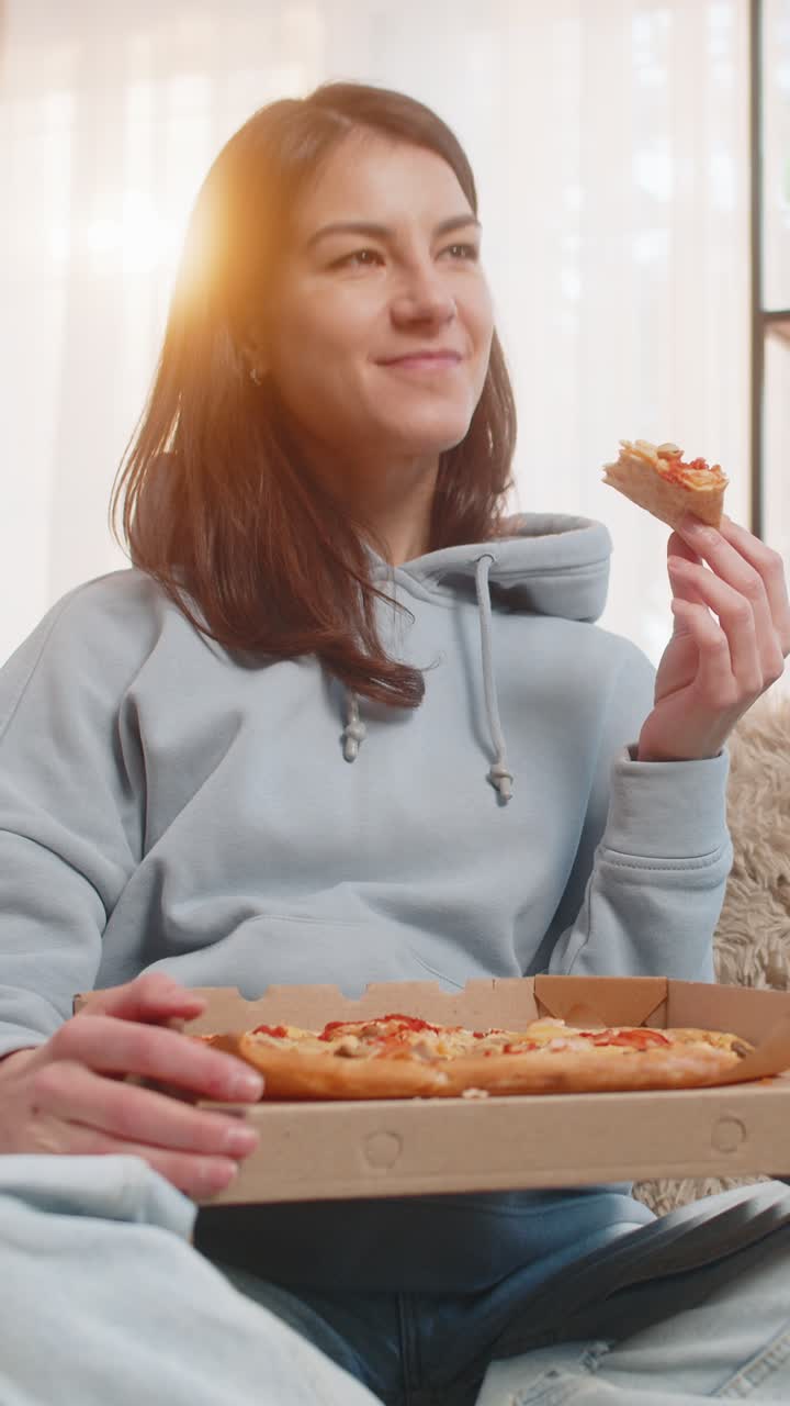 mujer joven comiendo deliciosa comida chatarra pizza y palomitas de maíz sentada en el sofá del sofá viendo la televisión en casa
