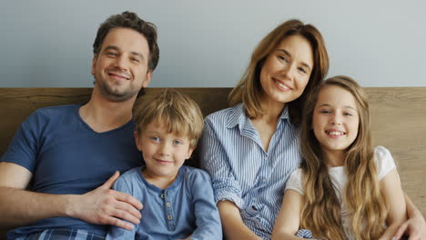 Cheerful-parents-and-their-sons-sitting-on-the-bed-and-talking-in-the-morning