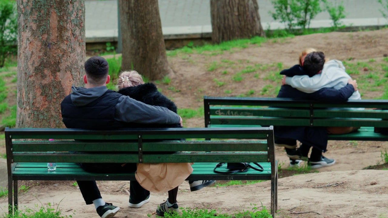 Et sløret billede af mennesker, der sidder på bænke i en park omgivet af træer.