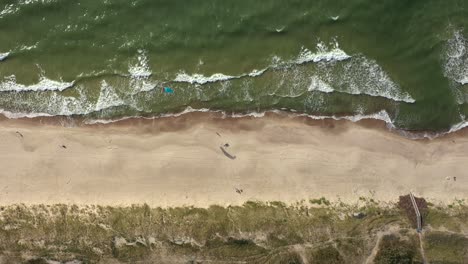 antena: vista superior de un surfista aislado con una cometa de viento parada en la playa con olas ondulantes