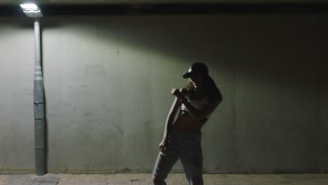 Mujer-Bailando-Joven-Bailarina-Practicando-Movimientos-De-Baile-De-Estilo-Libre-Moderno-Bajo-La-Luz-De-La-Calle-En-La-Ciudad-Por-La-Noche-Con-Sombrero