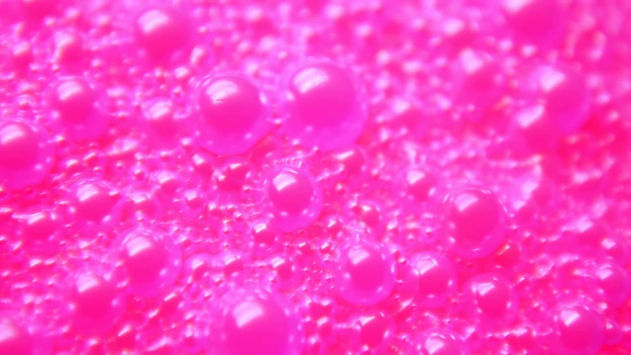 Vista macro di bolle rosa neon lucide raggruppate in densi ammassi, con sfere riflettenti, sfocatura morbida, sottile cambio di messa a fuoco, riflessi vividi e una vivace texture astratta su un'ampia superficie orizzontale.