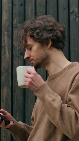 man drinking coffee and using a phone outside