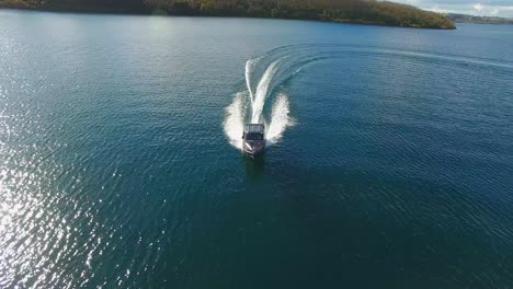 Toma-Aérea-Siguiendo-Un-Barco-Pesquero-Navegando-Rápido-En-Un-Gran-Lago-En-Nueva-Zelanda