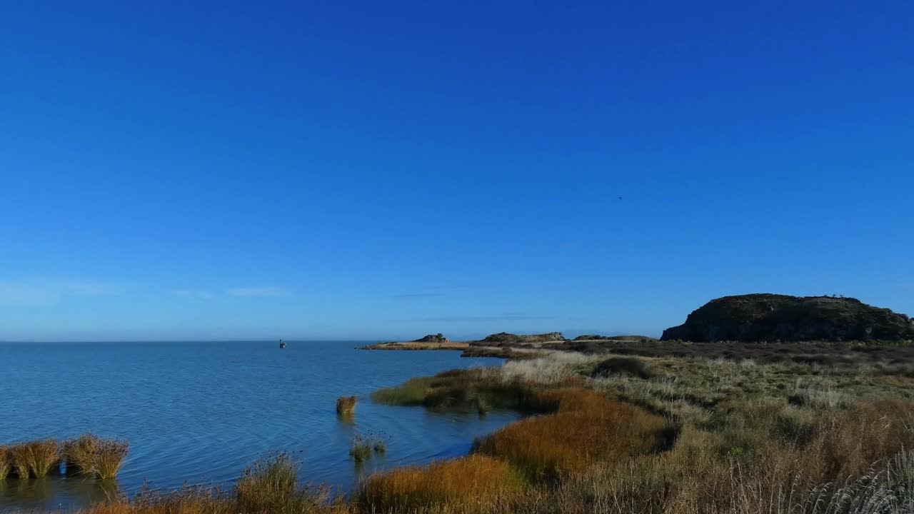 POV walking beside curve of deep-blue colored lake with gently lapping water on a beautiful, calm mid-winter's day (Lake Ellesmere, New Zealand)