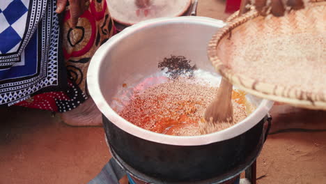 escena de cocina tradicional africana que muestra manos vertiendo sésamo en una olla