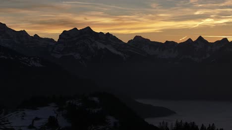 Dramatic-dusk-over-Amden-mountain-silhouettes,-Switzerland---aerial-panoramic