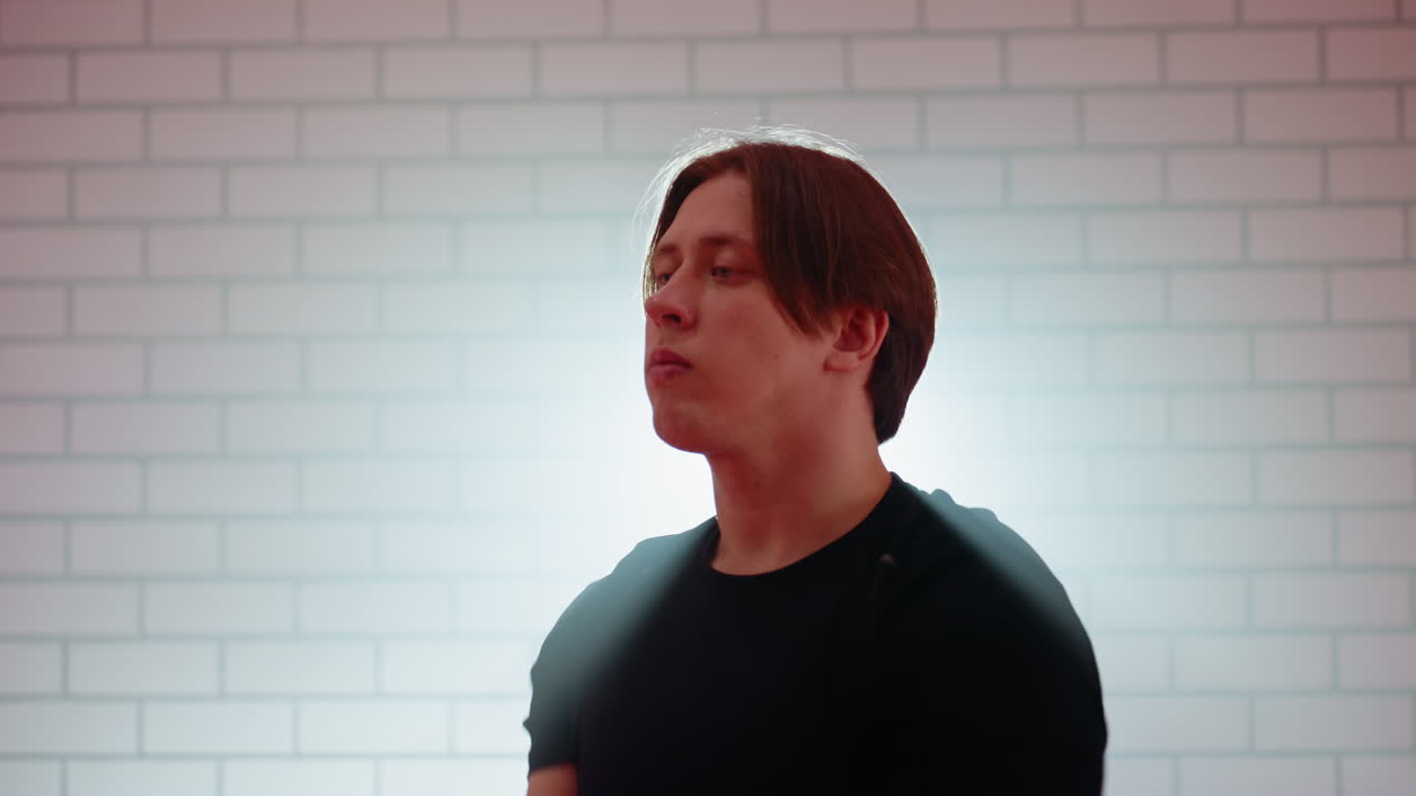 Young man in black shirt stretching hand indoors against white brick wall, holding guard stance with one fist near chin and other hand striking upward, showing training, focus, and fighting technique