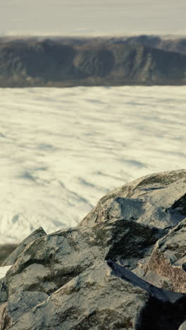 close-up of a glacier with rocks in the foreground and mountains in the background