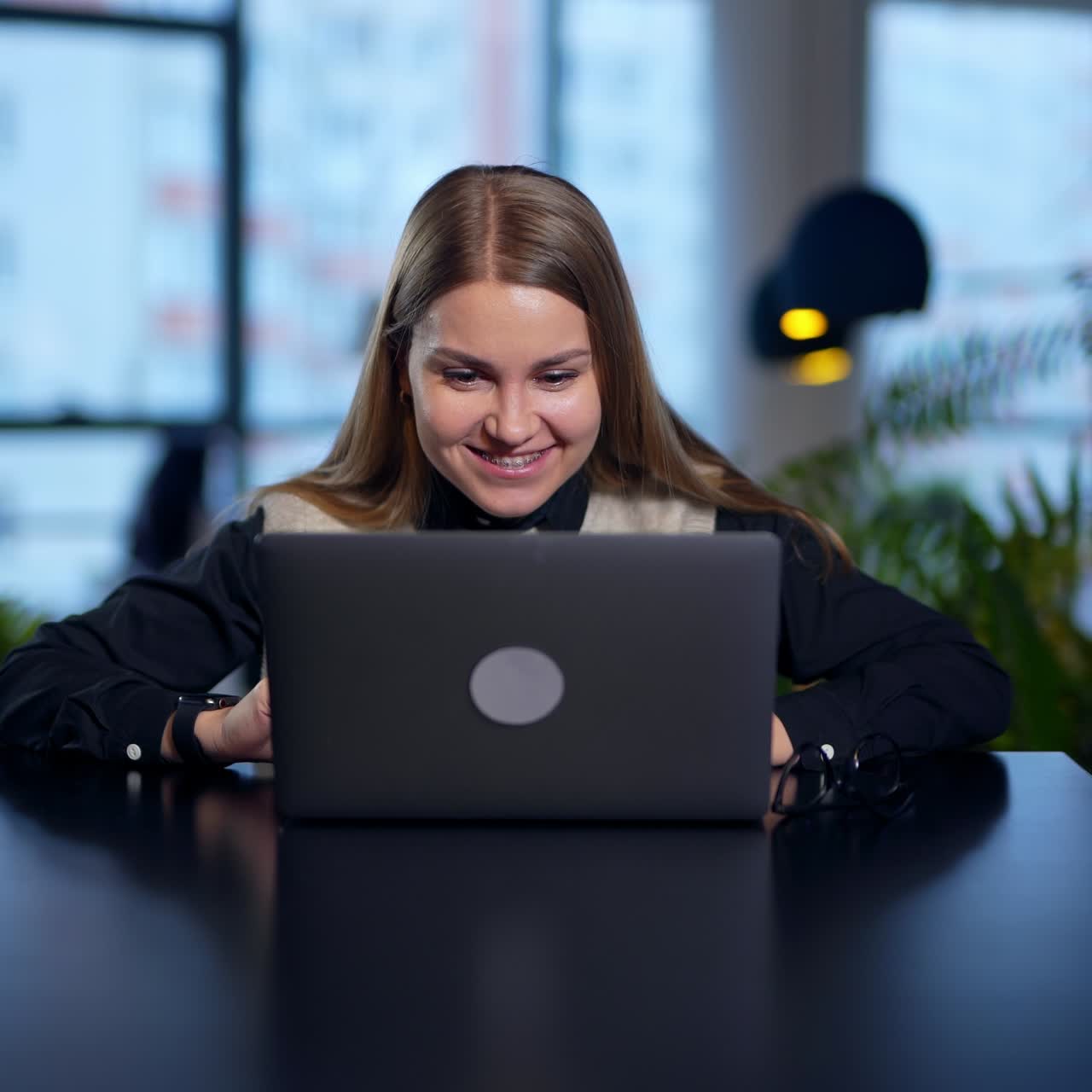 Good-looking young lady got the brilliant idea. Female employee opens a laptop, looks into it and then cheers about something