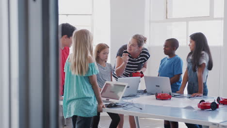 Estudiantes-Con-Profesora-En-Clase-De-Codificación-Informática-Después-De-La-Escuela-Aprendiendo-A-Programar-Vehículos-Robot