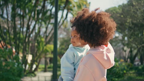 relaxed woman carrying child walking green park close up. curly mom strolling.