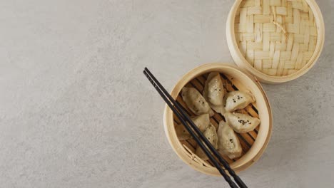 composition of bamboo steamer with gyoza dumplings and chopsticks on grey background