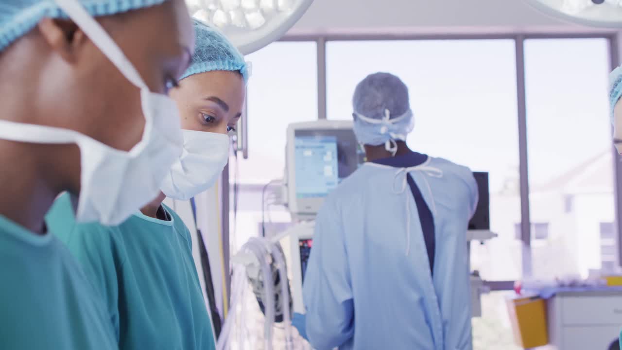 Video di tre chirurghe di diverse etnie che parlano durante un'operazione in sala operatoria, con spazio per il testo.