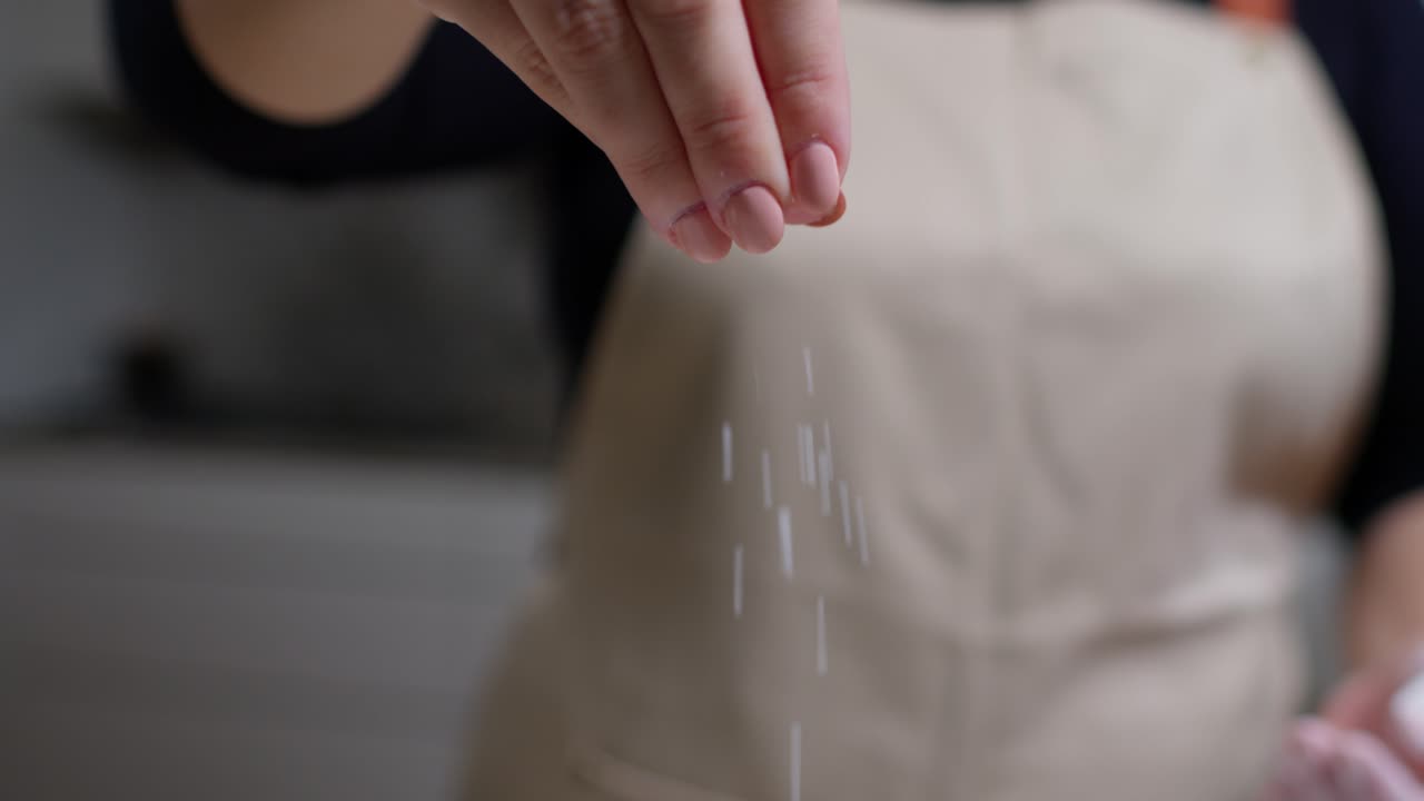 Hand sprinkling salt close up, adding seasoning for cooking in a kitchen.