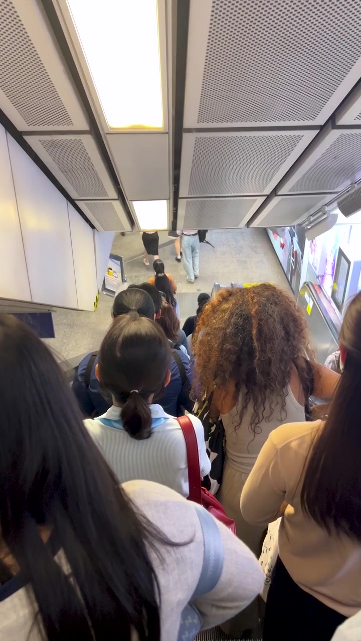 Penumpang turun dari eskalator yang ramai dalam pencahayaan dalam ruangan yang terang di stasiun transit Bangkok yang sibuk.