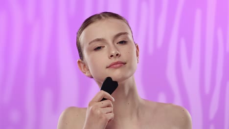 young woman using facial stone for skin care routine a young woman demonstrates a skincare routine using a facial stone tool set against a pink background