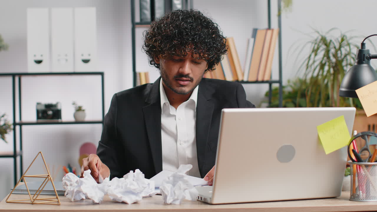 Angry furious man working at home office throwing crumpled paper having nervous breakdown at work